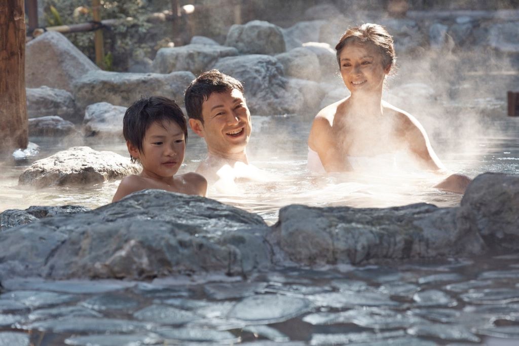 Two people relaxing in a traditional Japanese onsen, surrounded by nature, to promote muscle relaxation and body balance